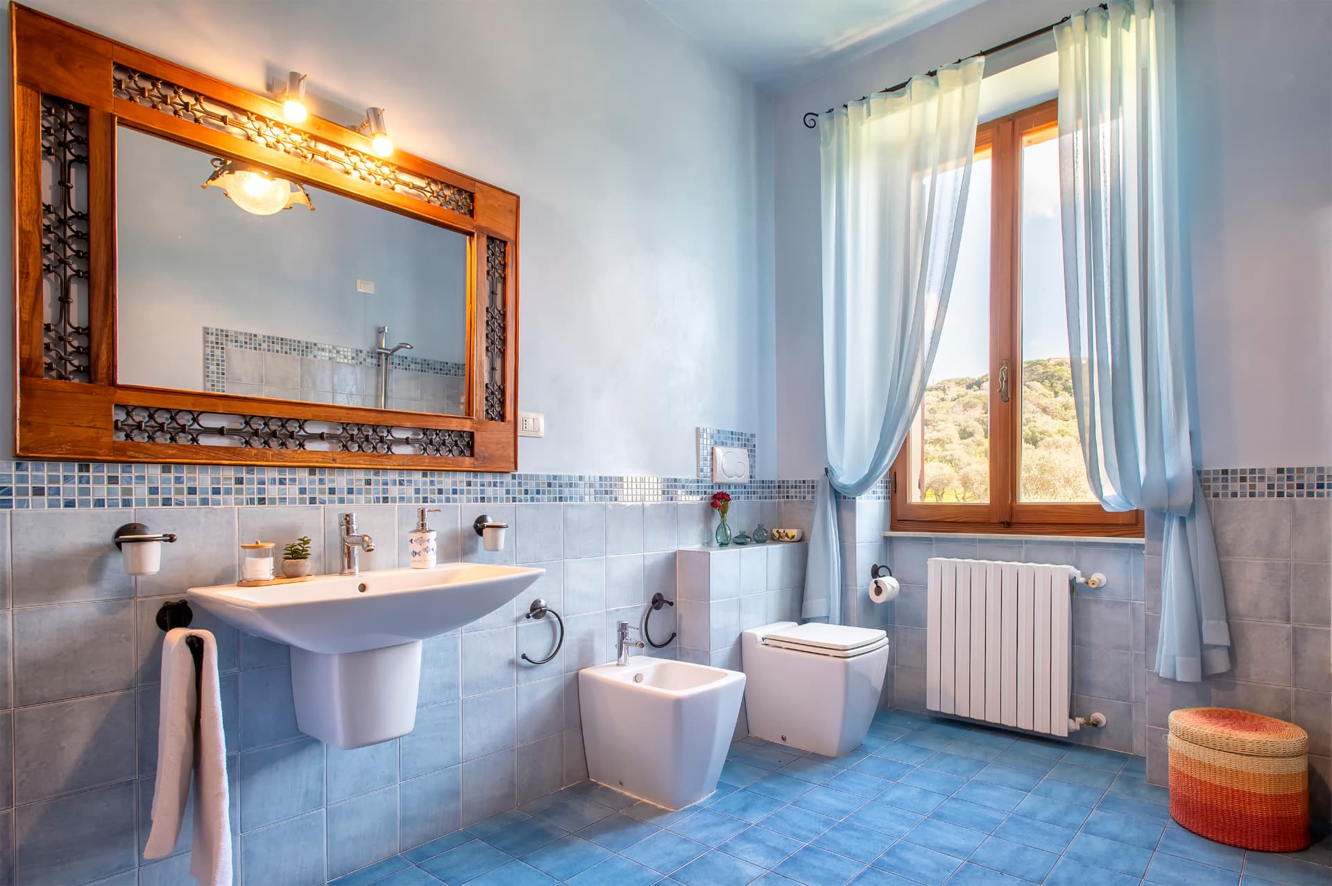 Il bagno azzurro con grande specchio in legno e vista sul verde